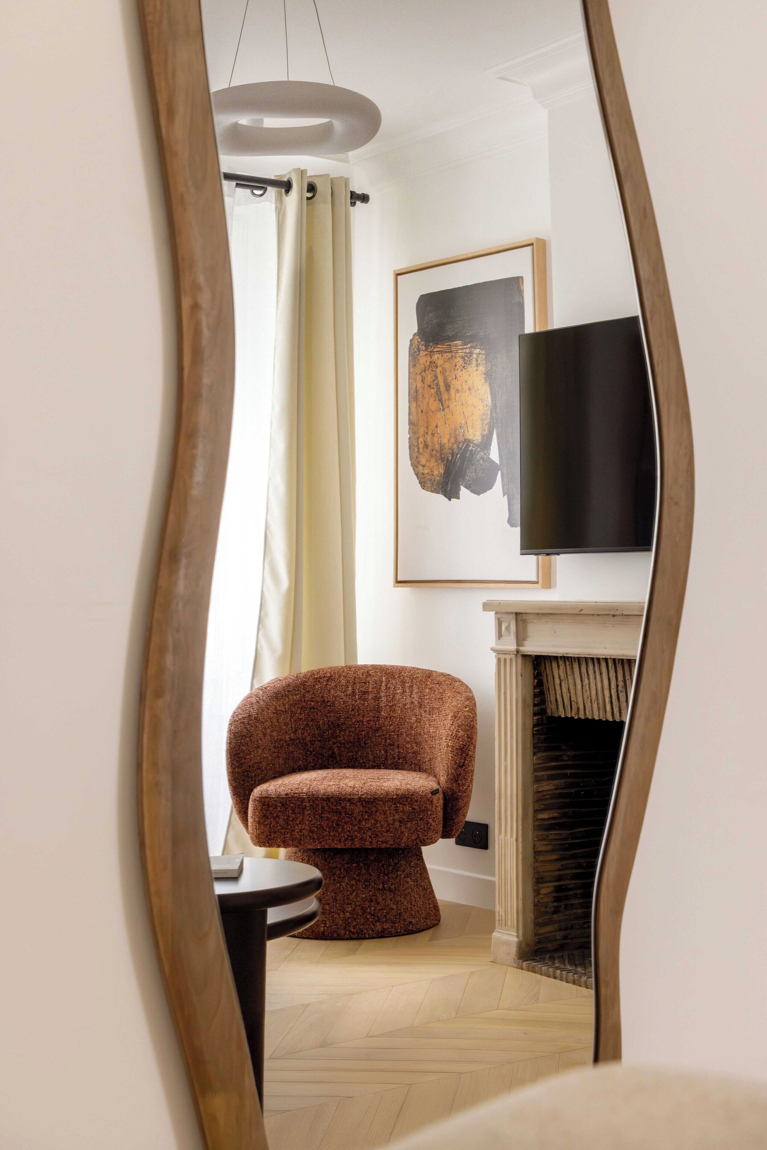 Une pièce avec un fauteuil marron, un téléviseur, une cheminée et un tableau accroché au mur.
