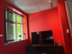A room with a large window, a flat-screen TV, and a red wall.