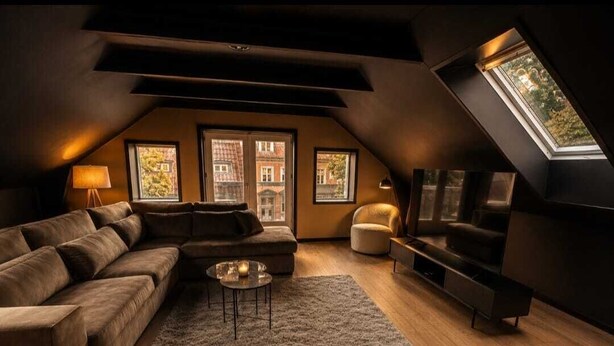 A loft-style living room with a sofa, coffee table, and TV stand, featuring a skylight and large windows. - Vermillion Autumn Suites (Aalborg)