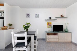 Un comedor con una mesa y sillas, un televisor sobre un mueble bajo y un armario con estantes.