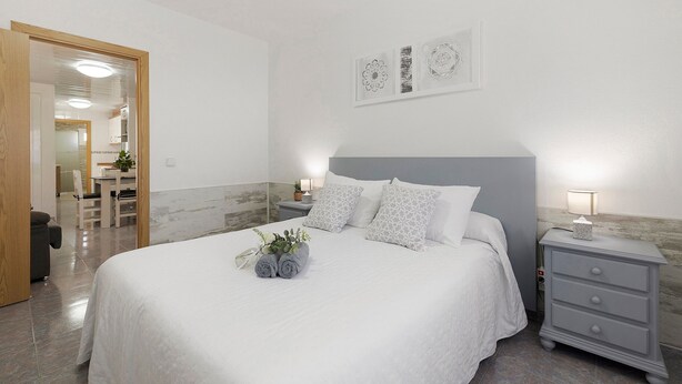 A neatly made bed with pillows, a bedside table with a lamp, and a wall with framed artwork. - Apartment 'Cristina' with Private Terrace, Wi-Fi, and Air Conditioning (Deltebre)