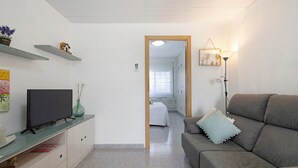 A living room with a sofa, a TV on a stand, a lamp, and a hallway leading to a bedroom. - Apartment 'Cristina' with Private Terrace, Wi-Fi, and Air Conditioning (Deltebre)