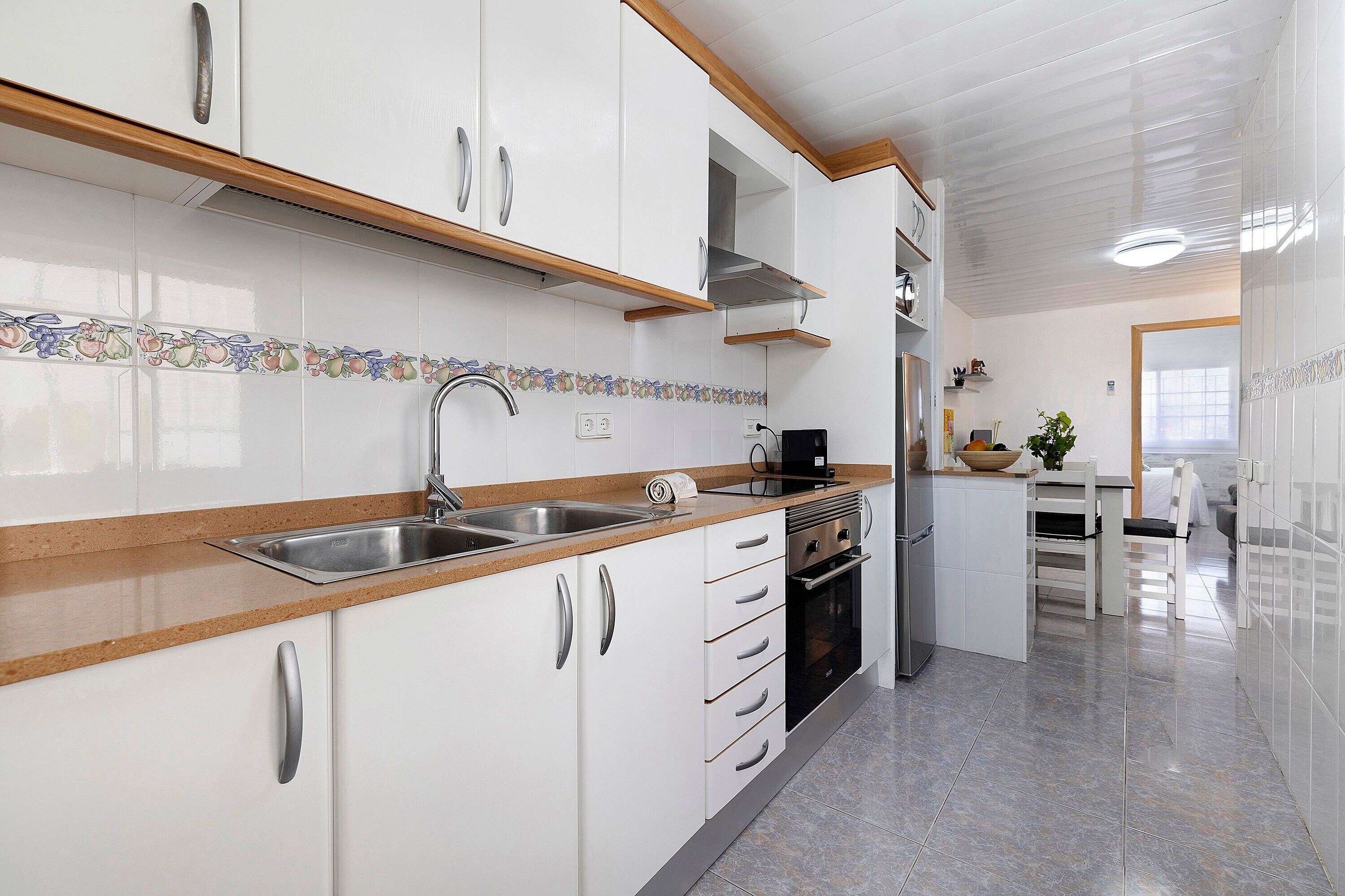Una cocina con gabinetes blancos, electrodomésticos de acero inoxidable, encimera de madera y salpicadero azulejado.