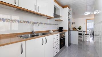 Una cocina con gabinetes blancos, electrodomésticos de acero inoxidable, encimera de madera y salpicadero azulejado.