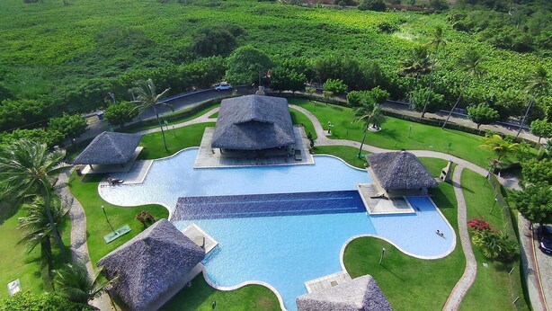 Ein gro ßer Pool mit ungewöhnlicher Form, umgeben von strohgedeckten Gebäuden und üppiger Vegetation.