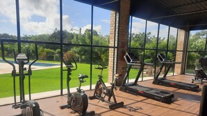 Ein Fitnessstudio mit verschiedenen Trainingsgeräten, großen Fenstern und Blick auf eine grüne Rasenfläche.