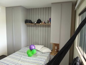 Ein Schlafzimmer mit einem Bett, Kissen, einem Regal mit Gegenständen und einem Fenster.