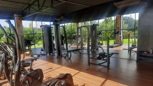 Ein Fitnessstudio mit unterschiedlichen Trainingsgeräten, großen Fenstern und Blick auf Grünflächen.