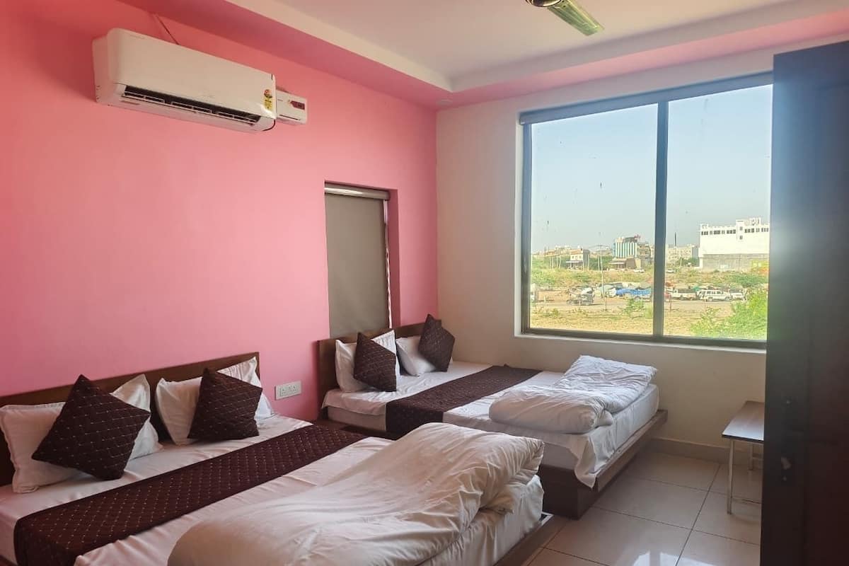A hotel room with pink walls, two beds, a window with a city view, and an air conditioning unit.