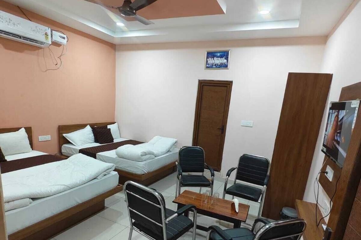 A hotel room with three beds, a desk with chairs, a ceiling fan, and a TV.