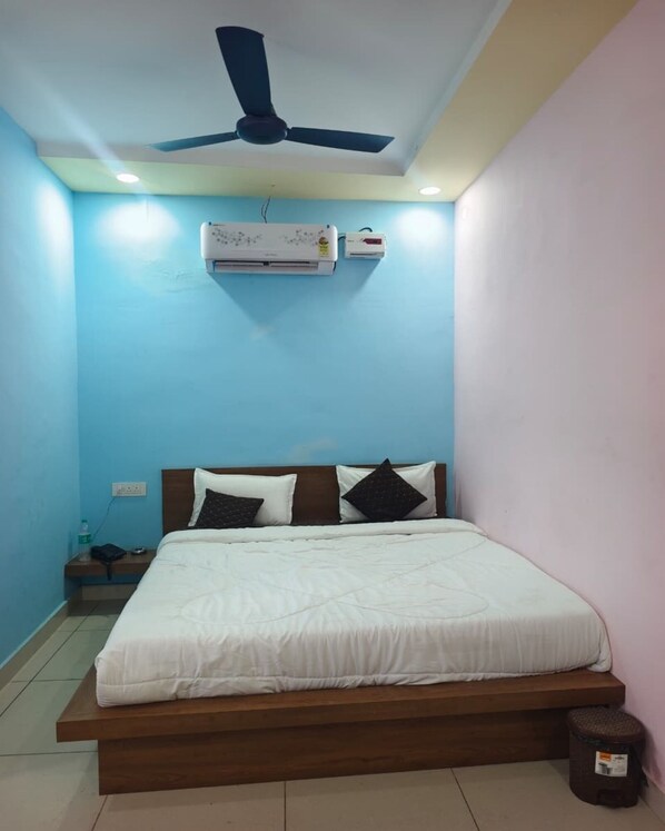 A bedroom with a bed, a ceiling fan, an air conditioner, and a nightstand. - DK HOTEL & RESTORENT (Phalodi)