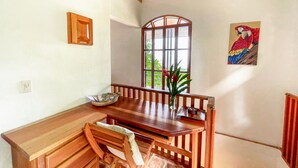 Uma área de refeições com mesa de madeira, cadeiras, janela com vista e um quadro na parede.