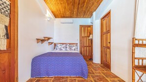 Quarto com cama, teto de madeira, chão de azulejos e porta de madeira.
