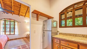 Uma cozinha com geladeira, armários de madeira, uma janela com cortinas e um ventilador de teto.
