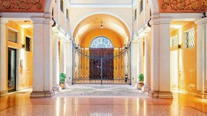 Un vaste hall d’entrée avec une porte cintrée au centre, des colonnes et un sol carrelé.