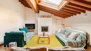 Un salon de style industriel, avec un plafond haut, des poutres en bois, une cheminée et un téléviseur.