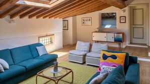 Un loft spacieux avec un plafond haut, des poutres apparentes, une lucarne, un canapé, un fauteuil, une petite table et un meuble.