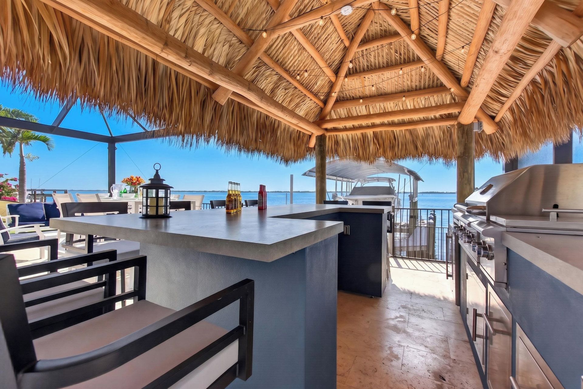 Un espace cuisine extérieur doté d’un toit de chaume, de tabourets de bar et offrant une vue sur la mer.