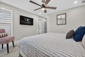 A bedroom with a bed, a ceiling fan, a wall-mounted TV, and a door leading to a bathroom. - VRCC Villa Pura Vida (Cape Coral)