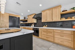 A modern kitchen with wooden cabinets, a black refrigerator, and a black stove. - VRCC Villa Pura Vida (Cape Coral)