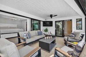 Un soggiorno moderno con un divano, un tavolino e poltrone. Si intravede una ventola a soffitto ed è presente un cartello di Vacation Rentals Cape Coral.