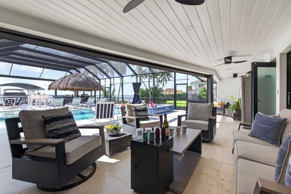 A modern outdoor lounge area with a pool, seating, and a view of the ocean. - VRCC Villa Pura Vida (Cape Coral)
