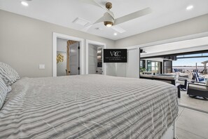 Una camera da letto moderna con un letto grande, un ventilatore a soffitto e vista su un balcone con mobili da esterno.