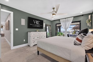 A bedroom with a bed, a ceiling fan, a TV on the wall, and a view of the outdoors. - VRCC Villa Pura Vida (Cape Coral)