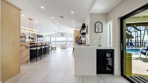 Une cuisine spacieuse avec un coin bar, une grande fenêtre donnant sur une piscine et une vue sur l’océan.