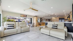Un salon moderne avec deux canapés, un ventilateur de plafond et une cuisine en arrière-plan.