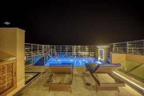 A rooftop pool area with lounge chairs, a pool, and a glass balustrade.