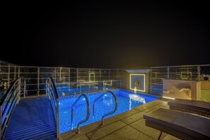 A rooftop pool with a glass barrier, a hot tub, and a set of stairs leading to the pool.