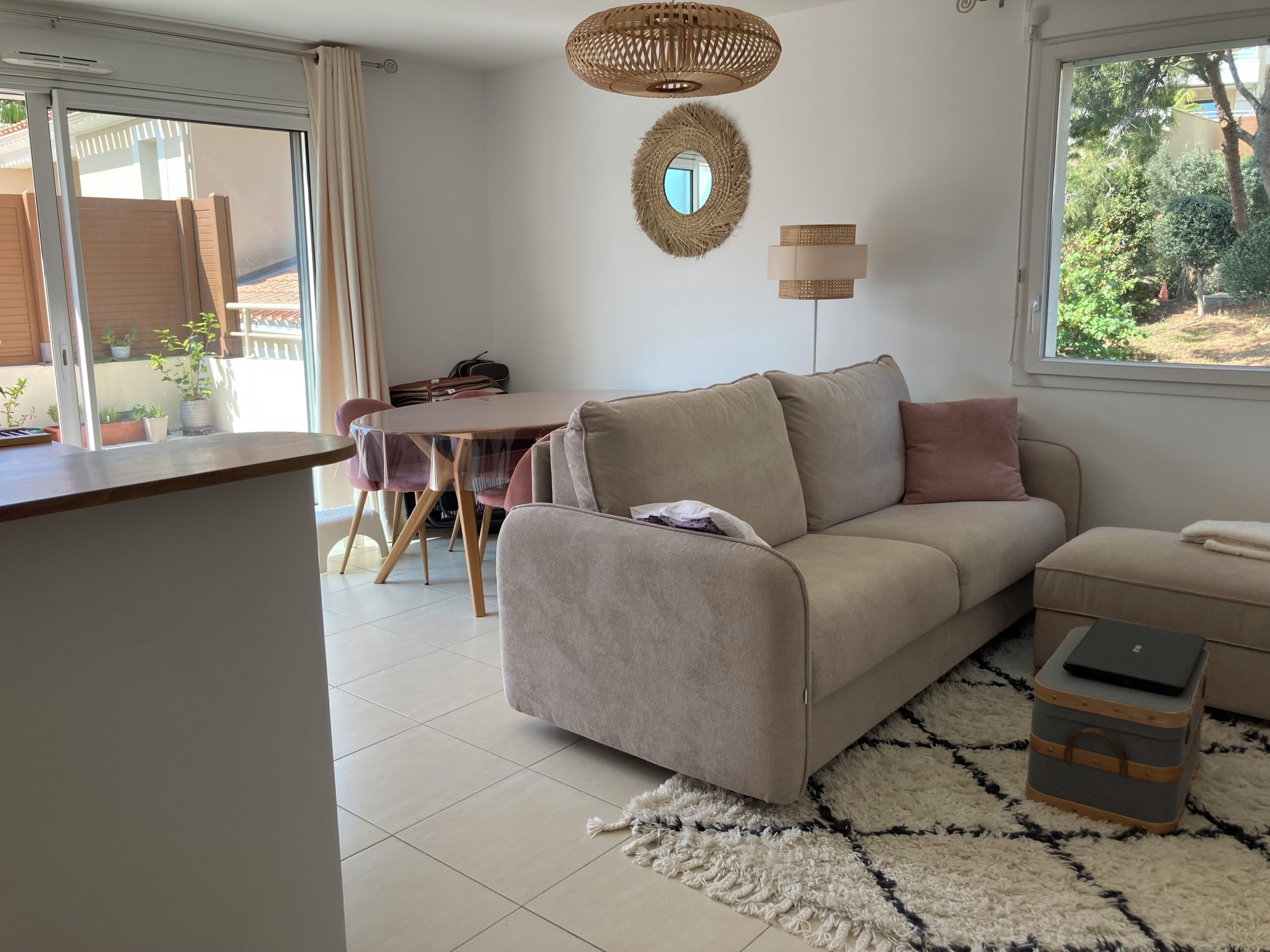A living room with a sofa, a dining table, and a window with a view of greenery.