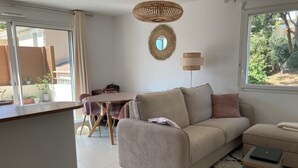 Una sala de estar con un sofá, una mesa de comedor y una ventana con vista a áreas verdes.