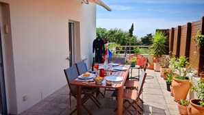 Un área de comedor al aire libre con una mesa lista para dos personas, rodeada de macetas con plantas y una valla de madera.
