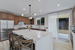 A modern kitchen with a central island, wooden cabinets, stainless steel appliances, and a large window.