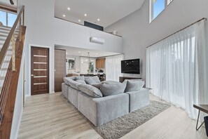 A modern living room with a grey sofa, wooden staircase, and a kitchen in the background.
