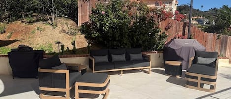 An outdoor patio area with a sofa set, a round table, and a covered grill.