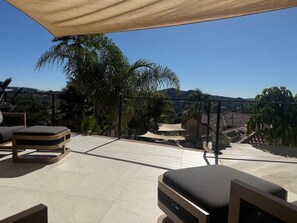 Un espace extérieur aménagé en terrasse, avec une table et des chaises, un coin salon abrité et une vue sur le paysage environnant.