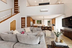 Ein großzügiger Wohnbereich mit einem grauen Ecksofa, einer Holztreppe und einer Küche im Hintergrund.