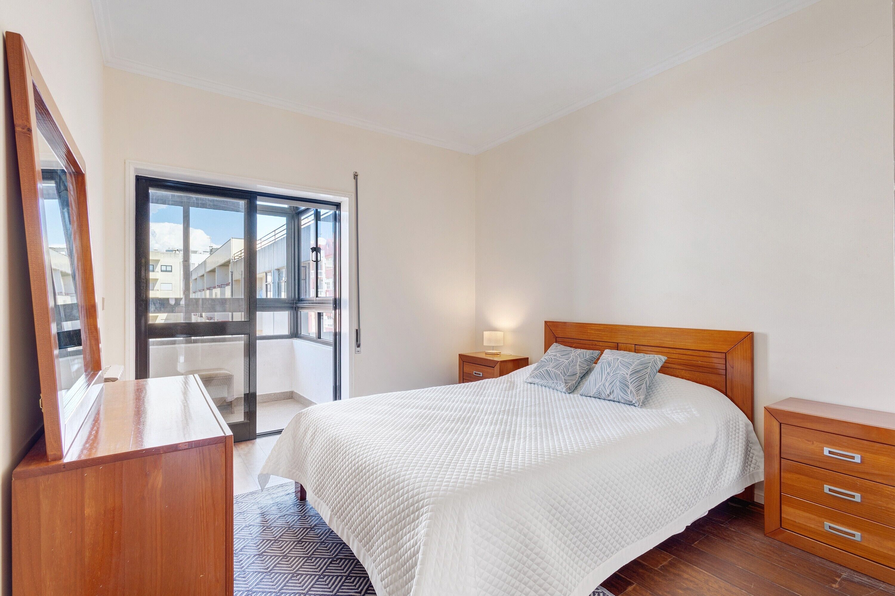 Une chambre à coucher comprenant un lit, des tables de chevet, une commode et une porte-fenêtre coulissante donnant sur un espace extérieur.
