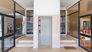 Vestíbulo moderno de edificio con puertas de vidrio, un ascensor central y piso de mármol.