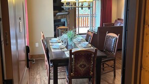 A dining area with a wooden table set for four, surrounded by chairs, a chandelier, and a view of a balcony. - Great Smokey Mountain Resort, condo Nestled between Gatlinburg & Pigeon Forge TN (Gatlinburg)