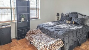 Un dormitorio con cama, banca, estante y ventana con persianas.
