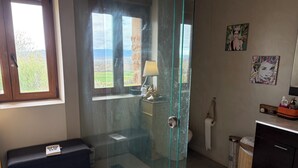 Kylpyhuoneessa on lasiseinäinen suihkukaappi, wc, pesuallas ja penkki.
