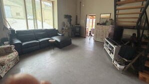 Tilava olohuone, jossa on musta nahkasohva, pieni pyöreä pöytä, televisio ja portaat.
