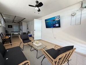 A living area with a television, wicker furniture, a ceiling fan, and a door leading to another room. - Humacao House with Lake and Beach (Punta Santiago)