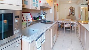 Een moderne keuken met roestvrijstalen apparatuur, een inbouwoven en een eethoek met een tafel en stoelen.