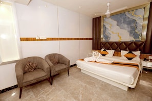 Una habitación de hotel con una cama grande, dos sillones, un cabecero de madera y un ventilador de techo.