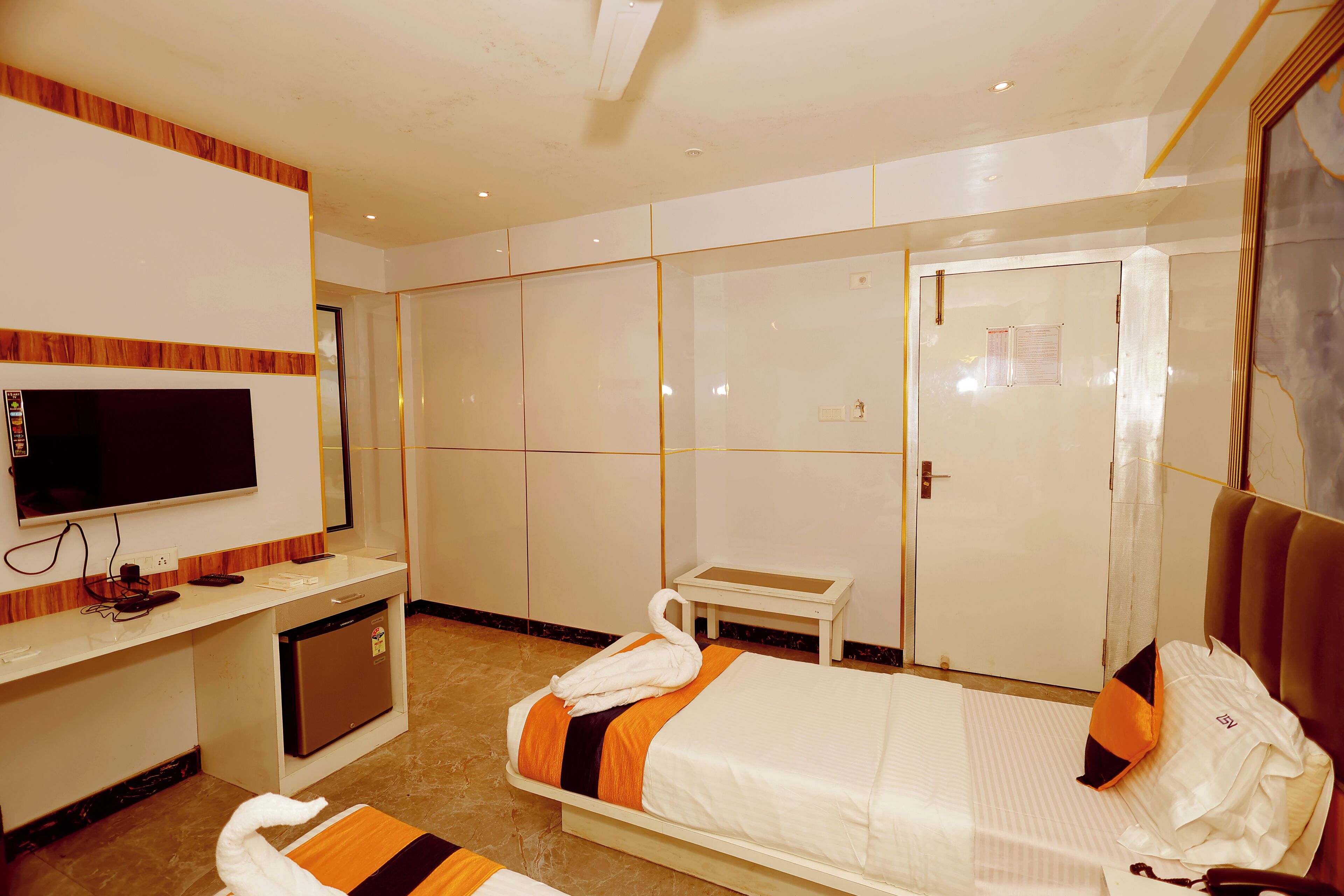 A hotel room with a bed, a TV, a desk with a computer, and a wardrobe.